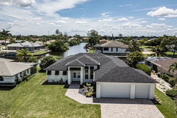 Aerial view of waterfront home with pool, dock, and canal in residential neighborhood with palm trees